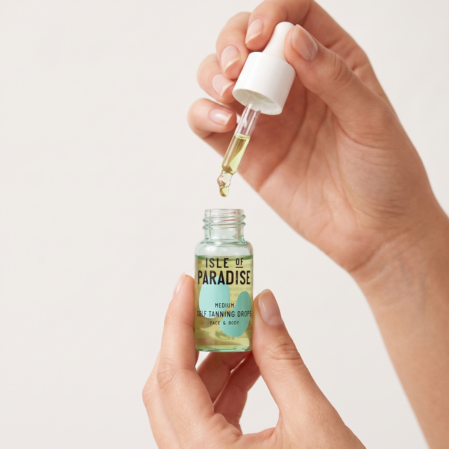 Hands holding Isle of Paradise Medium Self Tanning Drops mini bottle — Who should try these GOODS