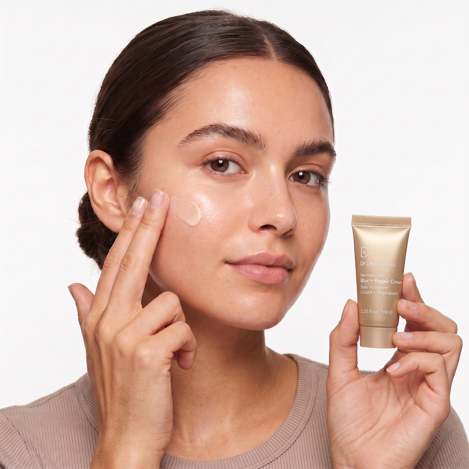 Who should try Dr. Dennis Gross DermInfusions Blur + Repair Cream — model blending the cream on her cheek holding the gold mini tube