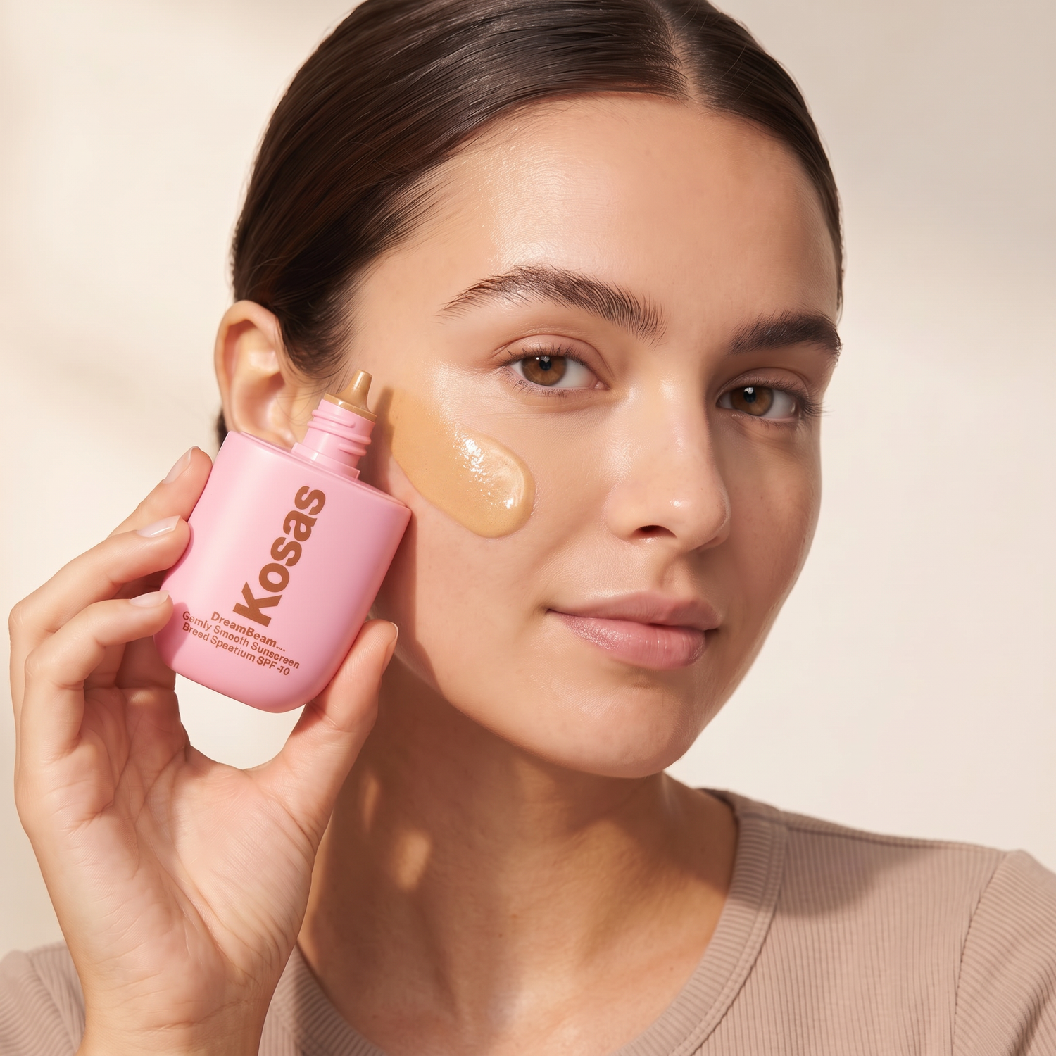 Who should try Kosas DreamBeam Sunlit SPF 40 — model with a golden sunlit glow holding the pink Kosas bottle